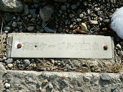 遊歩道脇にあった金属製の高圧ケーブル接続点を示すプレート