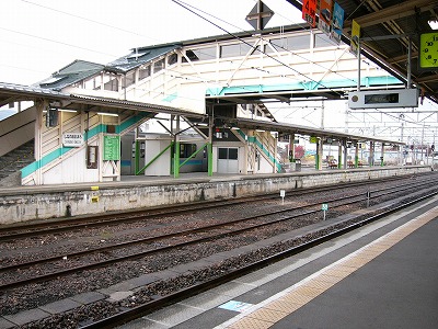 エメラルドグリーンのラインが施された跨線橋とホーム。下りのホームには銀色にラインの入った列車が停車