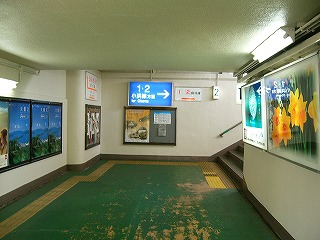 小浜線ホームへの短い回廊。突き当たりに先ほどの案内板があり、その右に階段ののぼりが顔を覗かせている。この回廊は入ってみると割と明るい。右手にはまたもや電照式広告灯<、左手にはずらっと並んだポスター。>cap