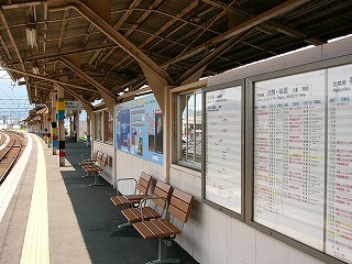 先10mぐらい続く風除け。風除けにはサッシの窓が嵌められ、額に入れられた時刻表が設置され、海と花火の写真の入った大きな広告が貼られてある。