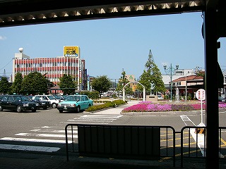 水色の空の下に、紅色の太いラインとガラスが交互になったビル、色とりどりの花の向こうにブロンズ像と噴水。