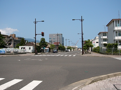 広くて大きな閑散とした交叉点。向こう側の建物はまばらで、電線もなく空が大きい。