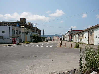 信号もない路面の傷んだ広い交叉点。向こう側には大橋の登り道が続いている。