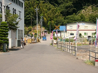 少し遠くに山肌。その手前に踏切。赤の幟が多数。