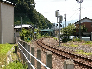 単線で遠くまで繊細にうねっている線路。左には急な山肌。右手には民家。