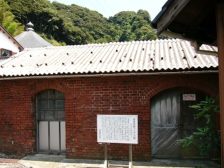 横長のレンガの建物。右に、上部がアーチになった木の扉、左にも上部がアーチになったガラスの窓。