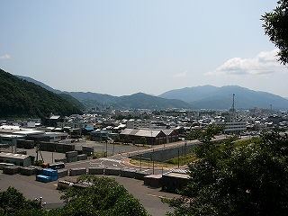 2車線道路のトンネル入口の上。アスファルトの広い敷地にコンテナが囲うように並べられてある。