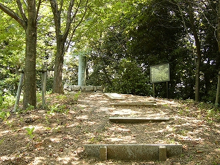 光差し込む薄い森の中、少し高い位置に石垣で囲われた太い柱が立っていて、文字が掘り込まれている。