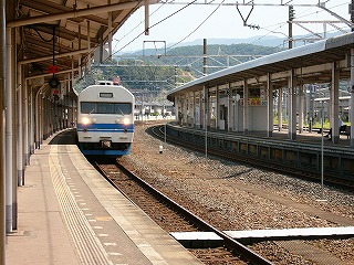 右側のホームはひと気がなく、遠くに湾曲して見え、今立っている4番線には乗ってきた419が停車している。背景には横長の山並み。南今庄方面を望む。