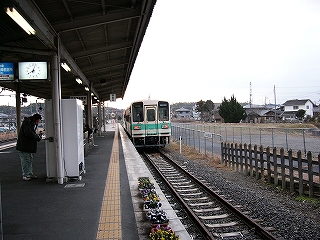 白地に明るいグリーンの太いラインの入った列車。ホームの手前の縁にはパンジーを植えたプランターがいくつか植えられている。