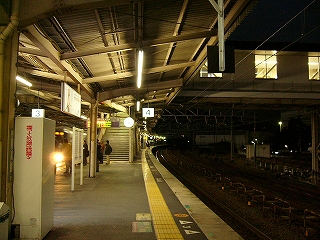 日の出前のホームに立って。右手に暗い線路内、ホームの奥の方にコンコースへの階段。ホームは蛍光灯がたくさんともり明るい。