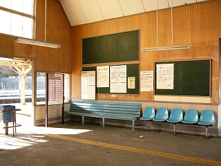 水色の長椅子が設置され、その背後には濃い緑色の掲示板が設置され、ポスターが貼られている。