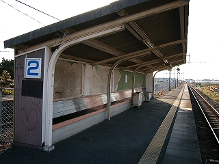 反りあがるような大きな屋根の付いた横に長い待合所。コンクリートの土台に木製の座る面が付けられた椅子が長く伸びている。