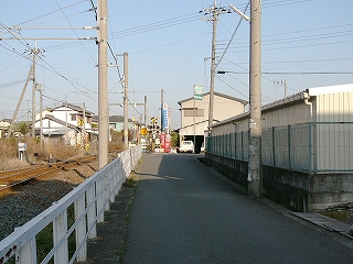 左手に白い柵、線路内、右手に白い倉庫。影の深い道を歩いて。