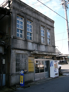 古いコンクリート造りの洋館風二階建ての建物。二階の窓は縦長で四つあり、それぞれ二列四段の正方形の格子で区切られてある。