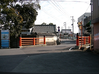 赤い欄干の短い橋。左手には寺らしい屋根がちらっと見えている。