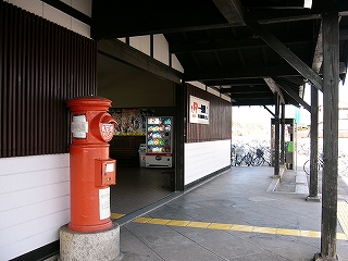 駅舎出口前の黒い回廊下から、駅舎出口を左斜めに見て。焦げ茶の桟と白い壁がりりしい。駅舎出口脇には赤丸ポストが設置されている。