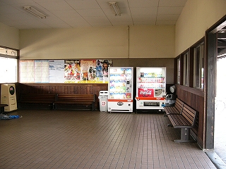 壁は下の部分が焦げ茶で、天井に近い部分が白色、天井は白色の駅舎内。左手の窓からは光が差し込み、右隅に自動販売機が二台ある。焦げ茶の壁に沿って焦げ茶の長椅子が置かれている。