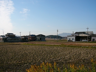 5,6軒の家々が固まる集落と土がむき出しの冬の田。空も青く冬の空になっている。
