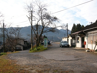 右手に駅舎があり、真中に冬枯れした大きな木のある駅前。駅前の舗装は半分くらいがはがれている。また、真中の木を取り囲むように、道が左に下っている。