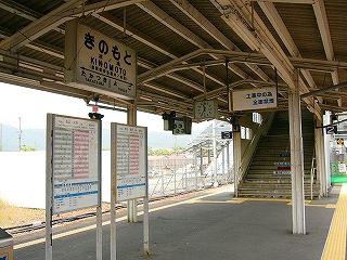 上屋から吊られた電照式国鉄駅名標とその下にあるホームに立てられた２つの時刻表。右手奥には階段上り口。