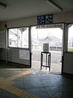 改札口を内側から見て。壁と天井は白色、地面は灰色のコンクリートで大きな菱形を詰め合わせたように見えるように線が入れられている。