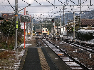スイッチバックで折り返して、上り線ホームへやって来る105系。右手には民家の垣根、そして民家の屋根が見えている。
