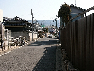1.5車線の住宅街の道。トタンで作った古い柵や真新しいアパート、個人の電器店が並ぶ。