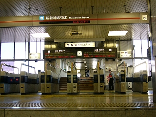 階段を上がりきる直前から見た、自動改札がずらりと並ぶ新幹線乗換改札。改札の並びの向こうには新幹線構内を渡るための跨線橋への低い階段が見えている。人は誰もいない。