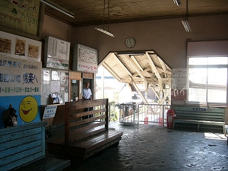 間口上部の左右の角がカットされた、ホームへの入口が奥にある駅舎内。天井が高く、床はぼこぼこのコンクリート。