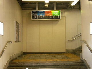 右に折れる階段の踊り場に4色で色分けされたホーム案内板が天井から吊られている。