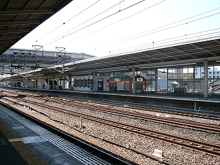 明るい線路内を挟んで、向かいの上り線ホームを右斜めに見て。先ほどのオレンジショップも見えている。