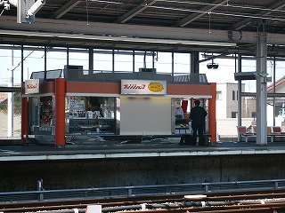 建物の4つの柱と天井部がオレンジ色に塗られてホーム上のお店。土台部分はステンレスになっている。