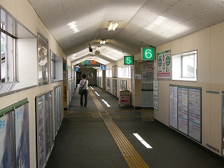 人が遠くに一人しかいない跨線橋内。両脇の壁の上部はサッシの窓が並んで設置されてあり、下部には額入りのポスターがずらりと貼り並べられている。