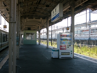 上屋の下に薄緑色に塗られた簡易な古い待合室を少し遠くから見て。写真手前右には自動販売機がホームの縁に寄せて立てられている。