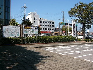 正方形の古いコンクリートが敷き詰められたバススペースの周りの乗降場。乗降場外縁の緑地帯のつつじの植え込みの中に大きな２つの看板が立てられている。