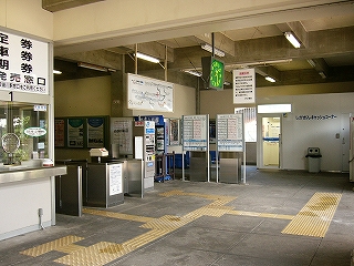 斜め左の位置に改札口、右奥に白い簡易な建物、天井はコンクリートが格子状に浮き立っている。