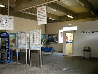 右奥に白い簡易な建物のキャッシュコーナー、その手前左手につい立式時刻表2つ。