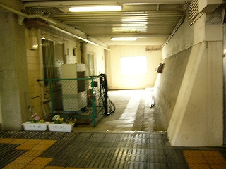 同じく三方を壁に囲まれた縦長のスペース。左手に緑のフェンスに囲まれた室外機。