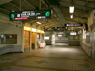 床は小さなタイル石張り、屋根からはフラップ式案内板が吊るされ、コンコースのような階段下り口付近。