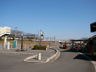 滑らかの曲線を描く縁石を持つ車一台分の幅の道。左手には時計と椅子と机のあるスペース。