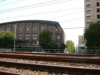 線路越しに見た濃いあずき色の体育館のような建物。