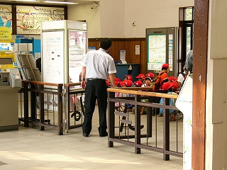 改札外に座って並ばされている赤い帽子をかぶった園児たち。