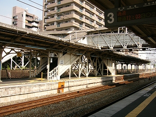 屋根のある上り線ホームを左斜めに見て。跨線橋の階段が二股に足を下ろしている。