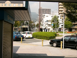 ロータリーの真中の一部の植え込みとタクシー。まっすぐ奥には信号があり、そこから閑散としたメインストリートが延びている。