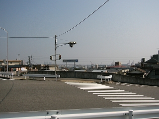 高架上の三叉路。信号の向こうは腰丈ぐらいの低いコンクリートの壁で、それより先には見下ろす街が広がり、ずっと遠くには赤と白のクレーンが何機も見える。