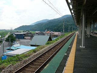 駅前の駐車場スペースの向こうに10件ぐらいの家。