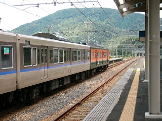 列車中ほどを先頭方向に見る。背景は鋭くない頂をもつ緑の山