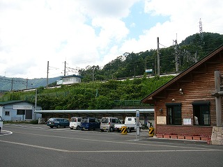 駅舎横の屋根つき駐車場。緑の盛り土の上に駅名標が覗く。