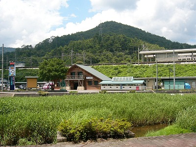 草むしたために浅く見える川向こうに2階建てのログハウス風の駅舎